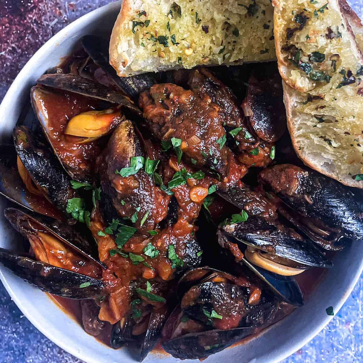 mussels in tomato sauce in a bowl with garlic bread